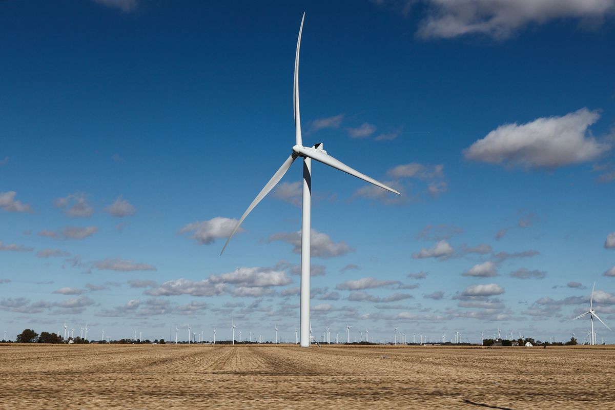 A white three-vaned wind turbine standing on a wide plain with blue sky and puffy clouds behind it.