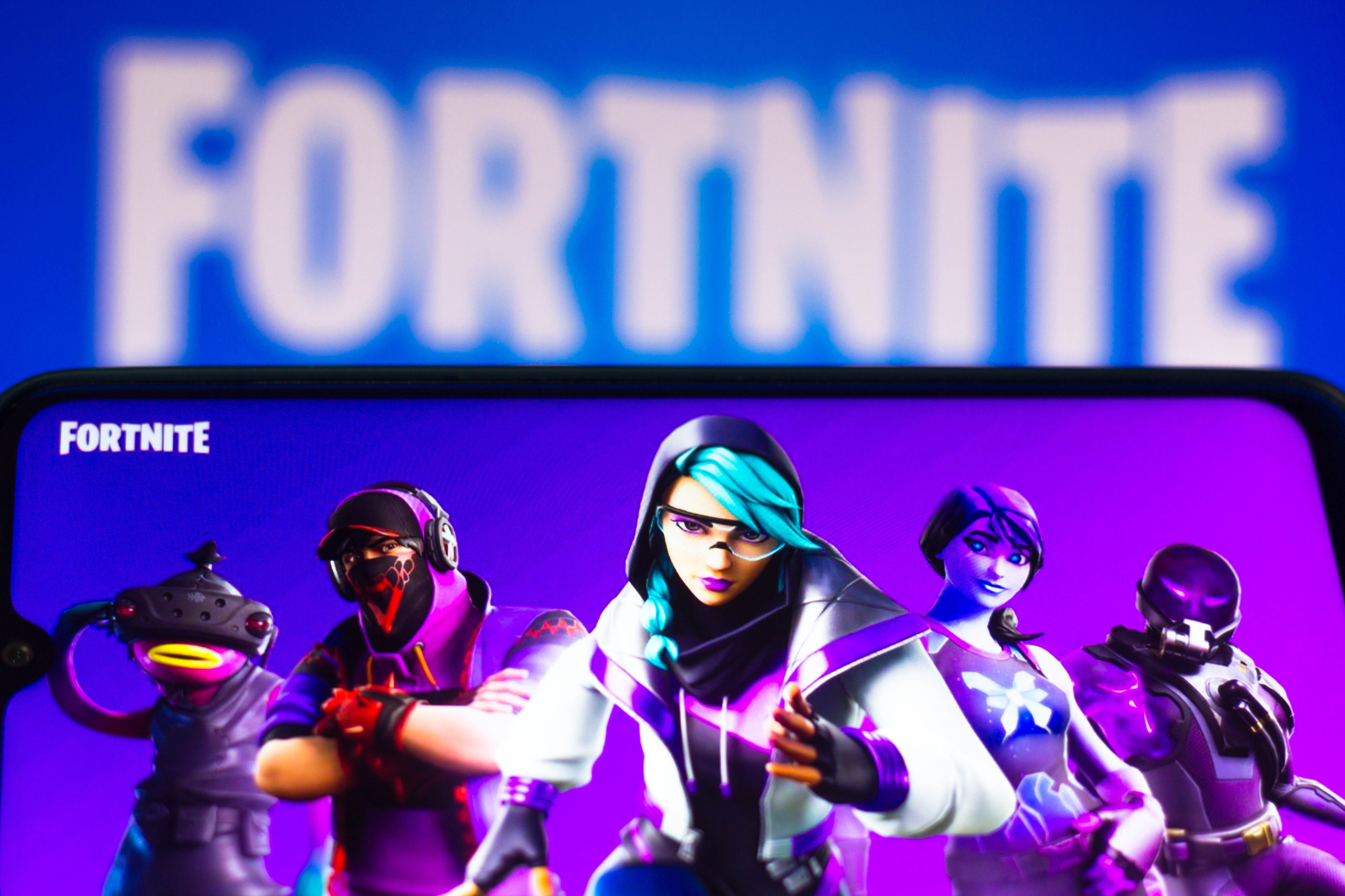 The Fortnite logo and avatars are seen on a smartphone and a computer screen.