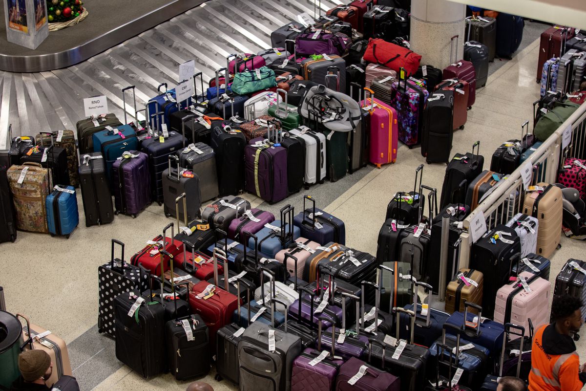 Dozens of suitcases are stacked around a baggage claim carousel.