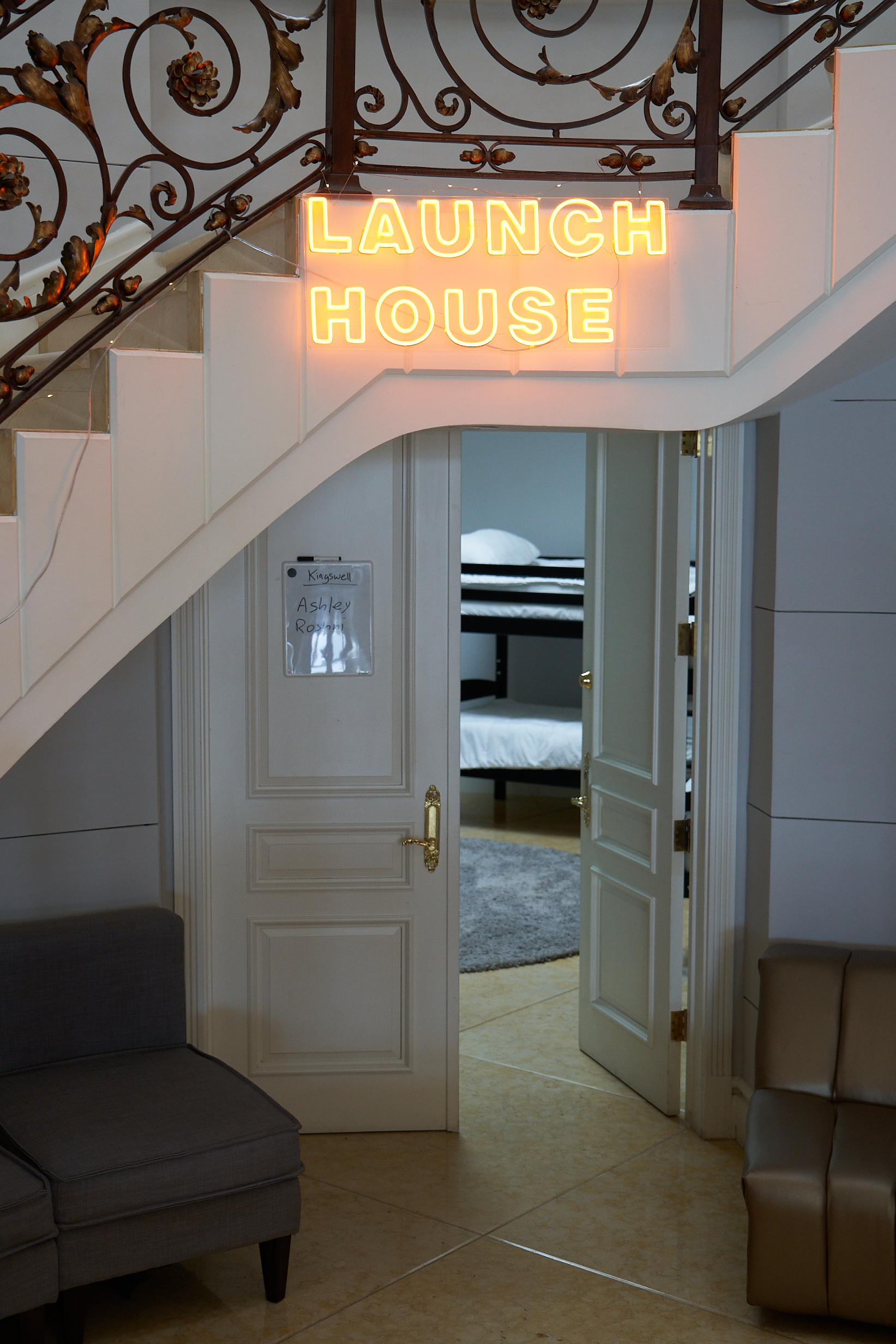 A neon sign that reads “Launch House” mounted on the side of an indoor staircase.